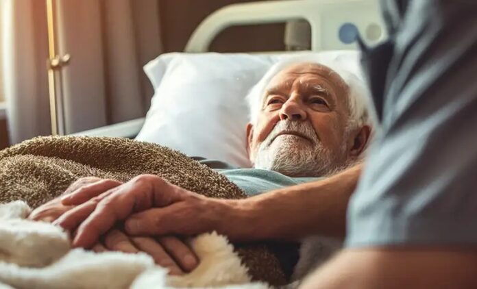 Oudere mannelijke patiënt in verpleeghuis. Verzorgende staat erbij.