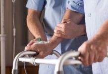 handen aan een looprek, met ondersteunende handen van een zorgverlener erbij