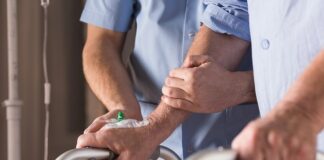 handen aan een looprek, met ondersteunende handen van een zorgverlener erbij