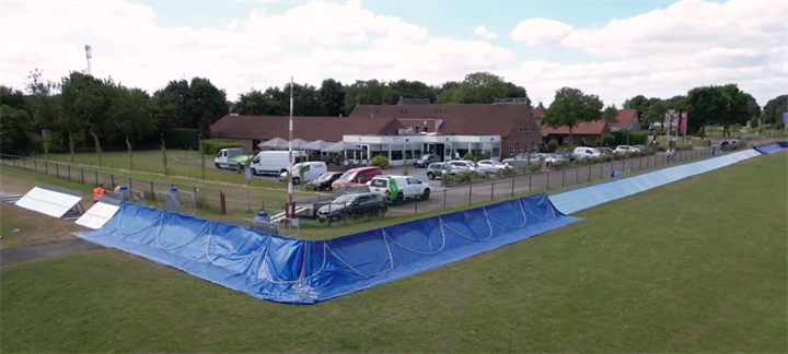 Een proefstuk van de tijdelijke waterkering op grasland bij het MUMC+. De metalen elementen zijn afgedekt met blauw folie.