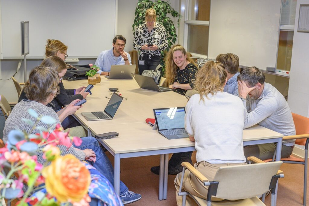 Negen onderzoekers van de flashmobstudie met smartphones en laptops rond een tafel.