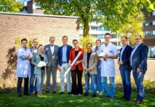 vertegenwoordigers van alle bouwpartners poseren buiten op een grasveld voor een muur