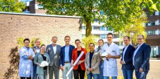 vertegenwoordigers van alle bouwpartners poseren buiten op een grasveld voor een muur