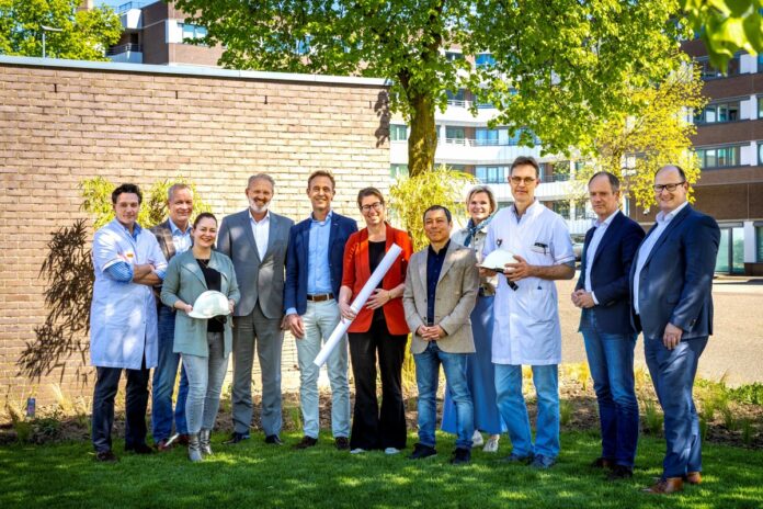 vertegenwoordigers van alle bouwpartners poseren buiten op een grasveld voor een muur